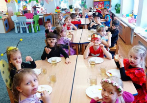 Dzieci siedzą przy stolikach i jedzą śniadanie